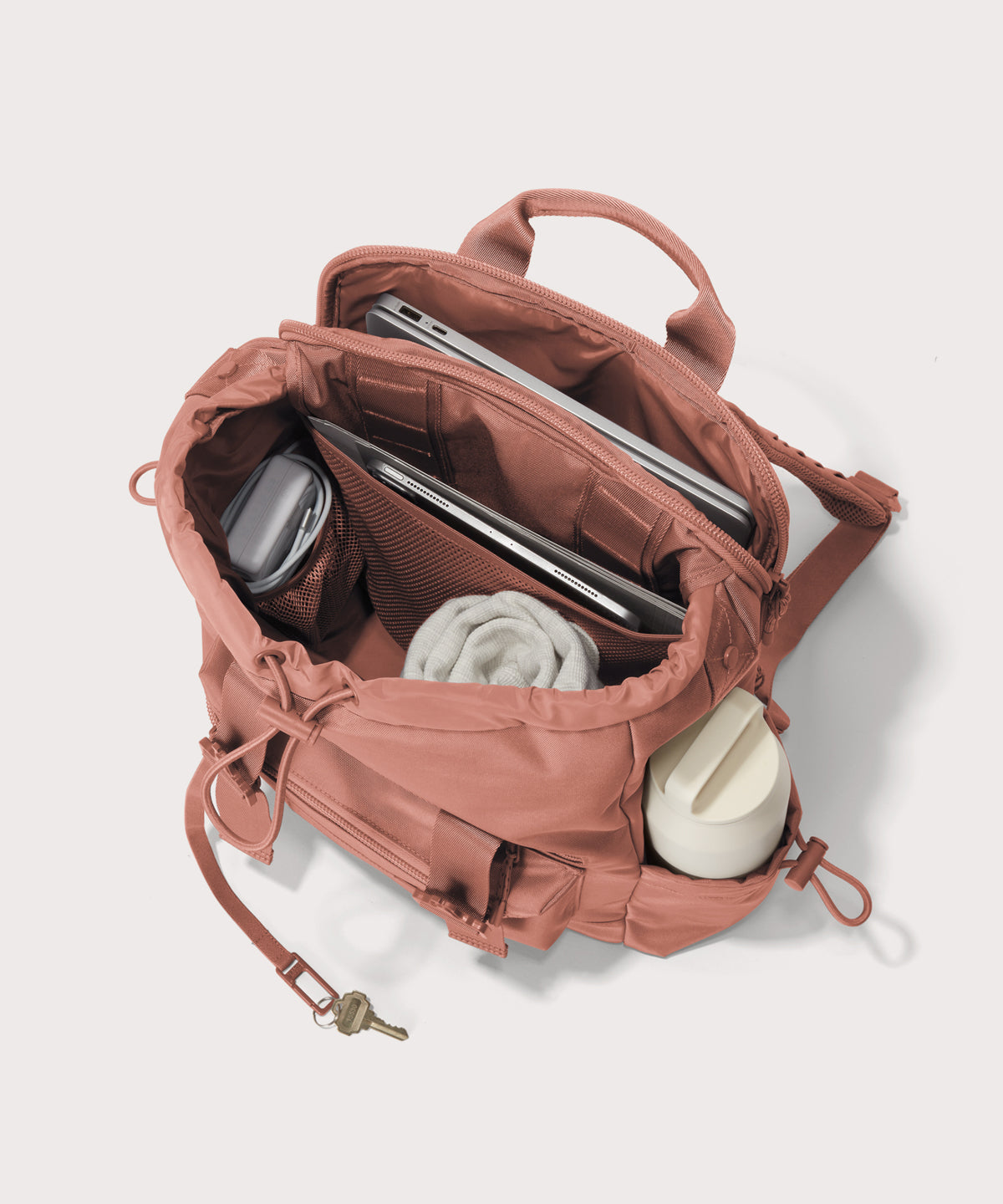 Pink backpack with compartments containing a laptop, water bottle, and other items on a light gray background