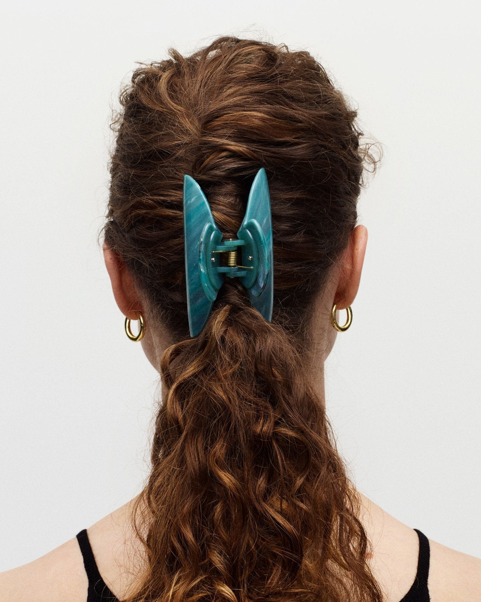 Person with teal hair clip in ponytail on plain background