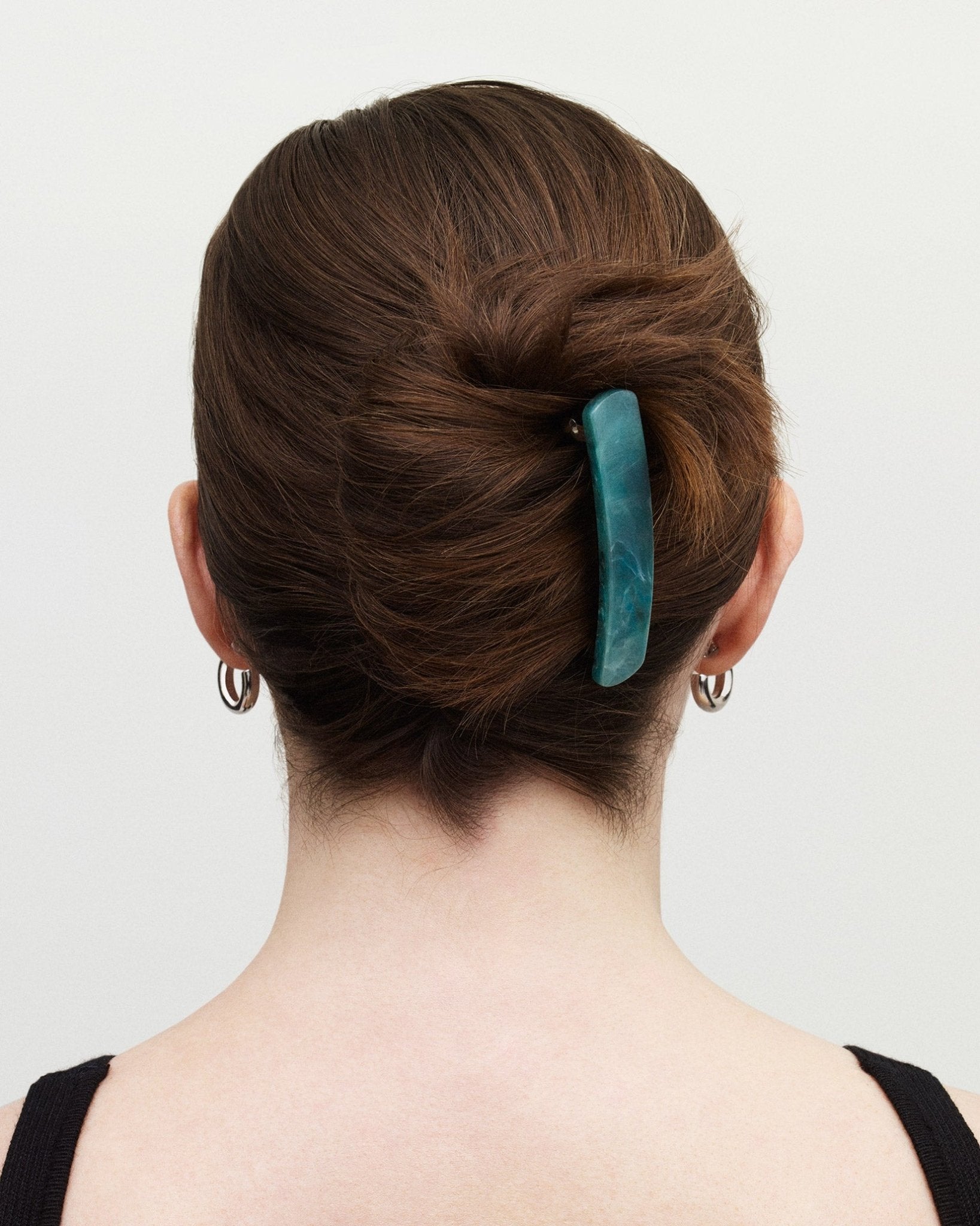 Person with a stylish hair bun holding a teal hair accessory against a plain background
