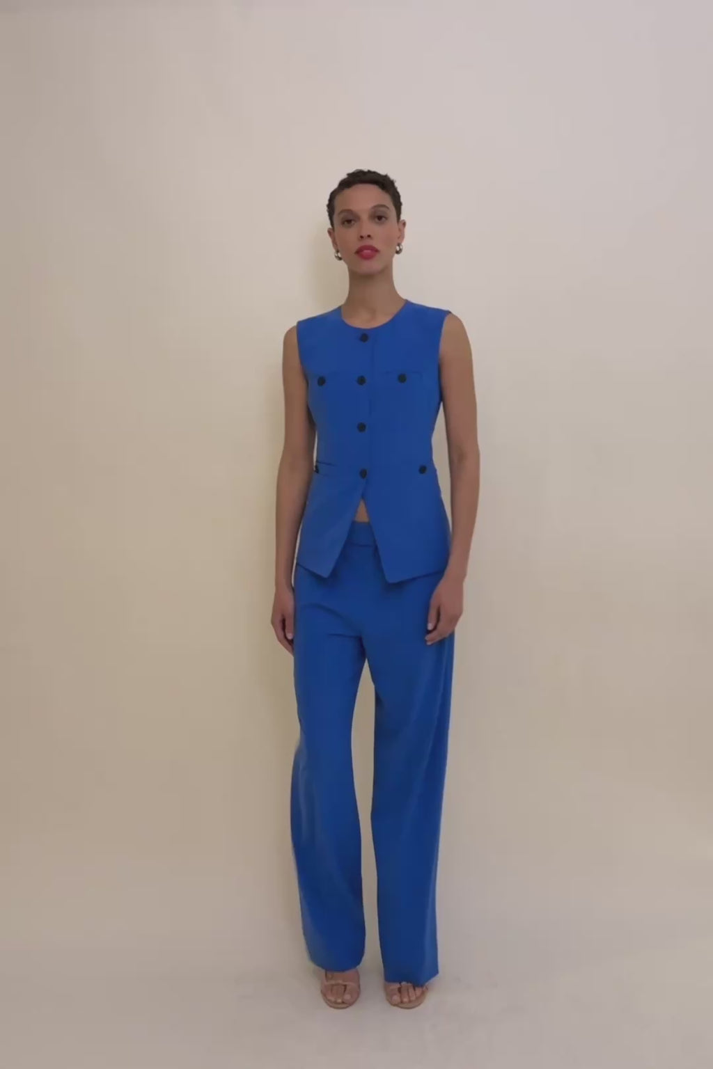 Woman wearing a blue vest with black buttons on a beige background 