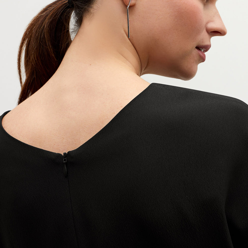 Front image of a woman standing wearing the Nejvi top in black