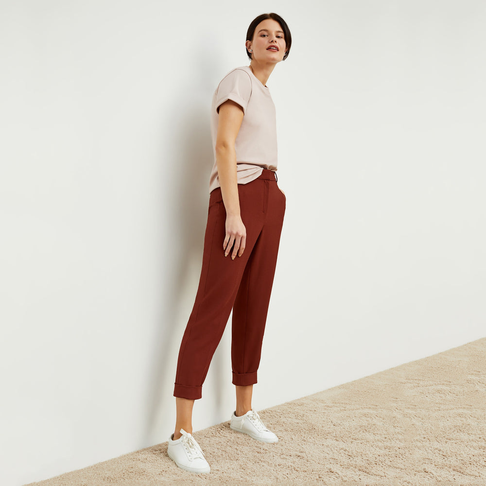 Side image of a woman standing wearing the mejia pant in sharkskin in rust