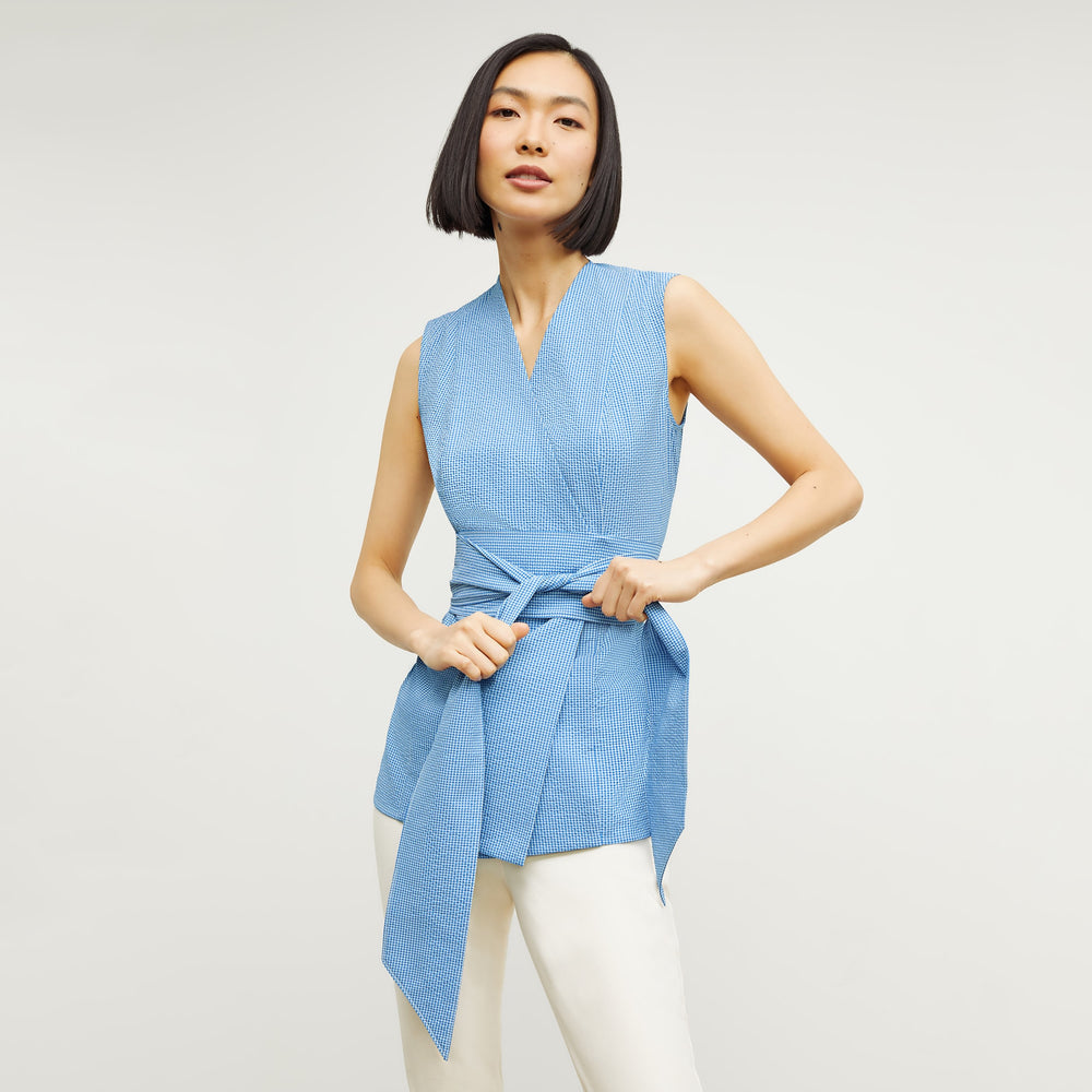 Front image of a woman standing wearing the ellen top in gingham seersucker in capri blue and white