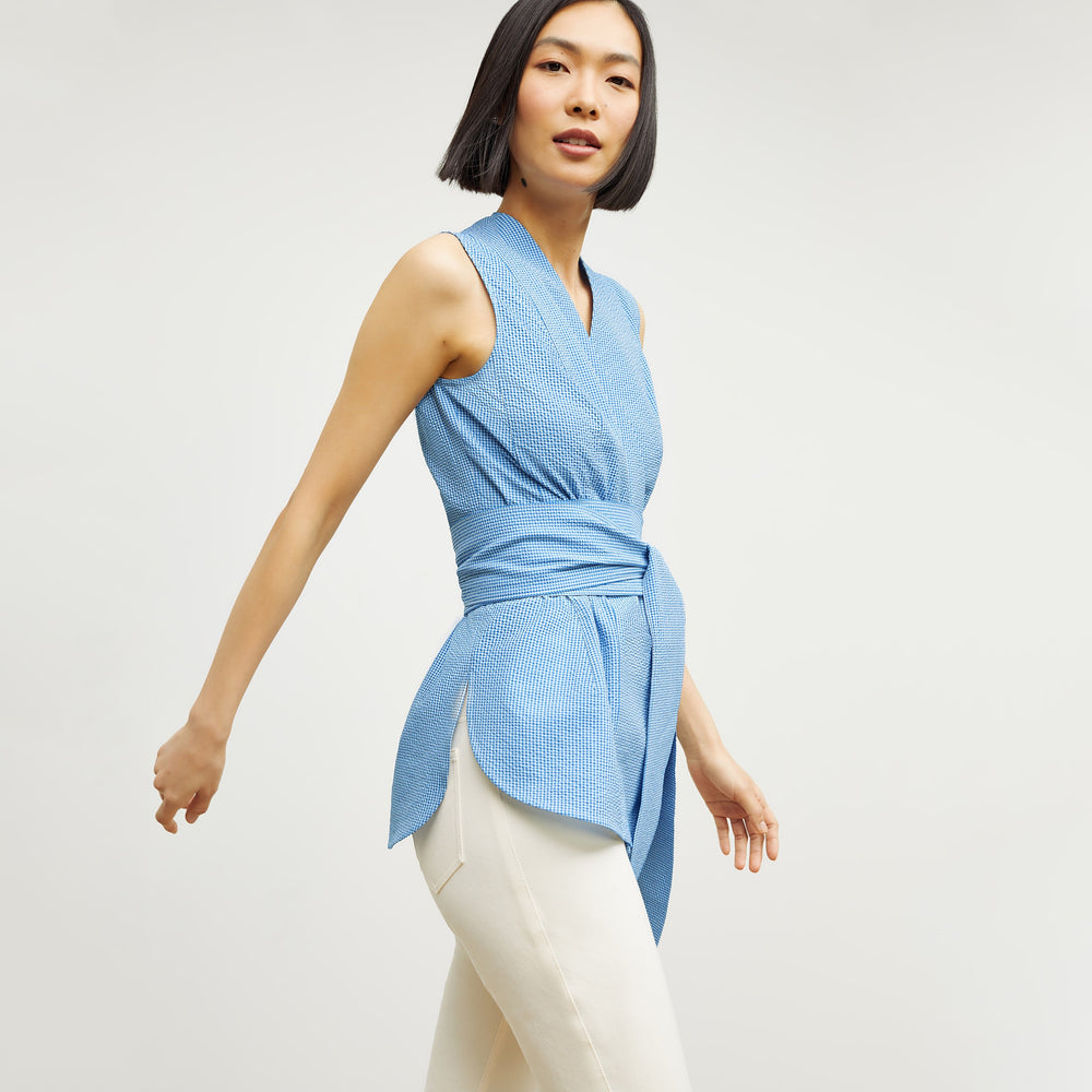 Side image of a woman standing wearing the ellen top in gingham seersucker in capri blue and white